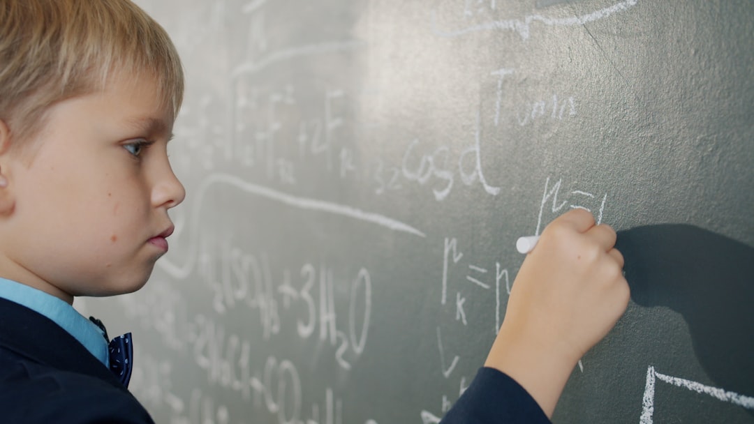 smart schoolboy writing formulas on chalkboard studying alone indoors busy with scientific calculations. People and education concept.