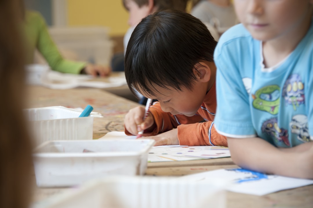 Captured in a metropolitan Atlanta, Georgia primary school, seated amongst his classmates, this photograph depicts a young Asian-American schoolboy, who was in the process of drawing with a pencil on a piece of white paper atop a table that had been covered by a layer of removable brown paper. Note how focused and intent he was on creating his artwork, seemingly oblivious to all the classroom goings-on that surrounded him. It is important to know that objects, including pencils, crayons, paper, etc., are known as fomites, and act as transmitters of illnesses. 