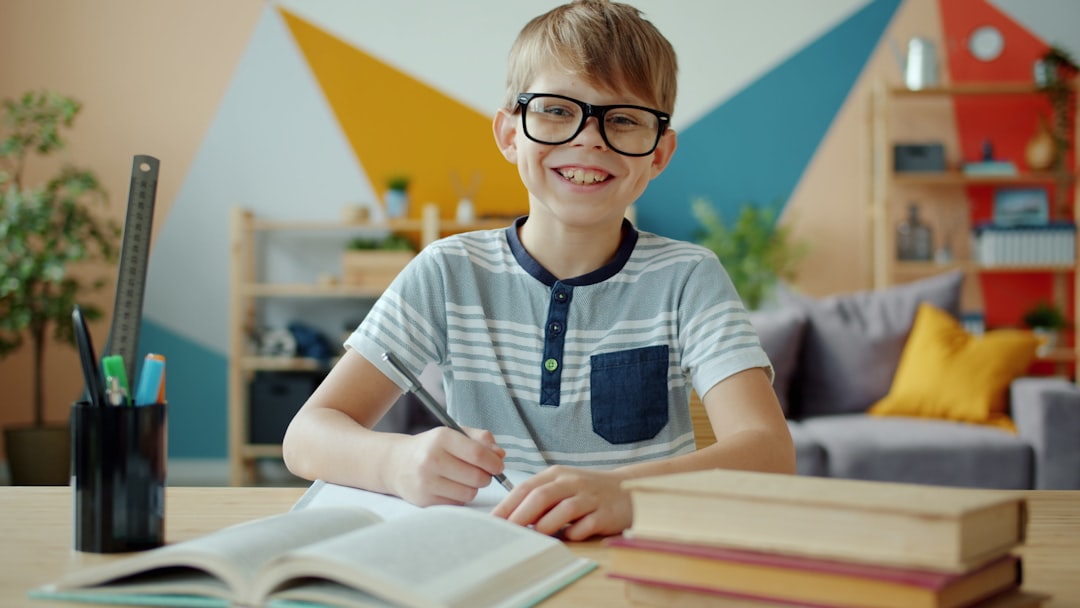 Portrait of joyful kid smiling laughing looking at camera doing homework indoors in apartment. Happiness, positive emotions and lifestyle concept.